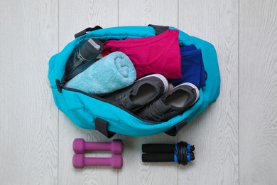 Photo of Bag with different sports equipment on wooden floor, flat lay