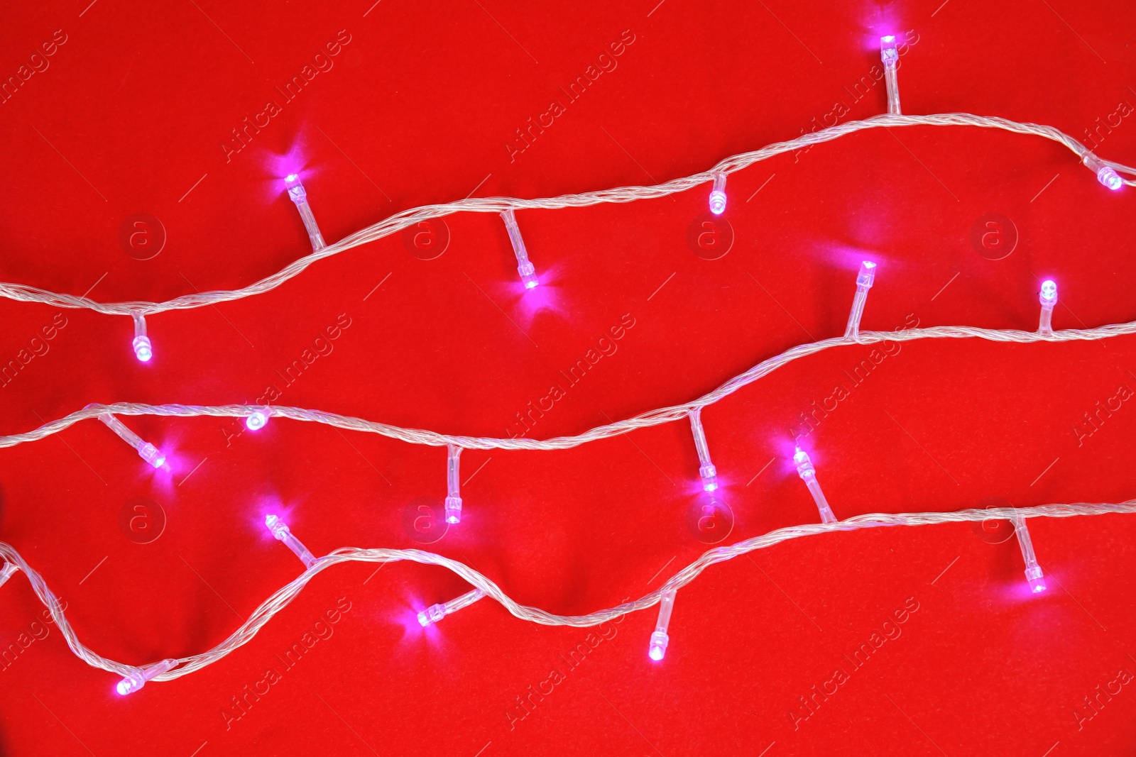 Photo of Glowing Christmas lights on color background, top view