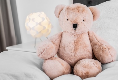 Photo of Cute teddy bear sitting on bed indoors. Space for text