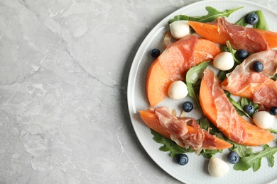 Photo of Fresh melon with prosciutto, mozzarella and arugula on light grey table, above view. Space for text