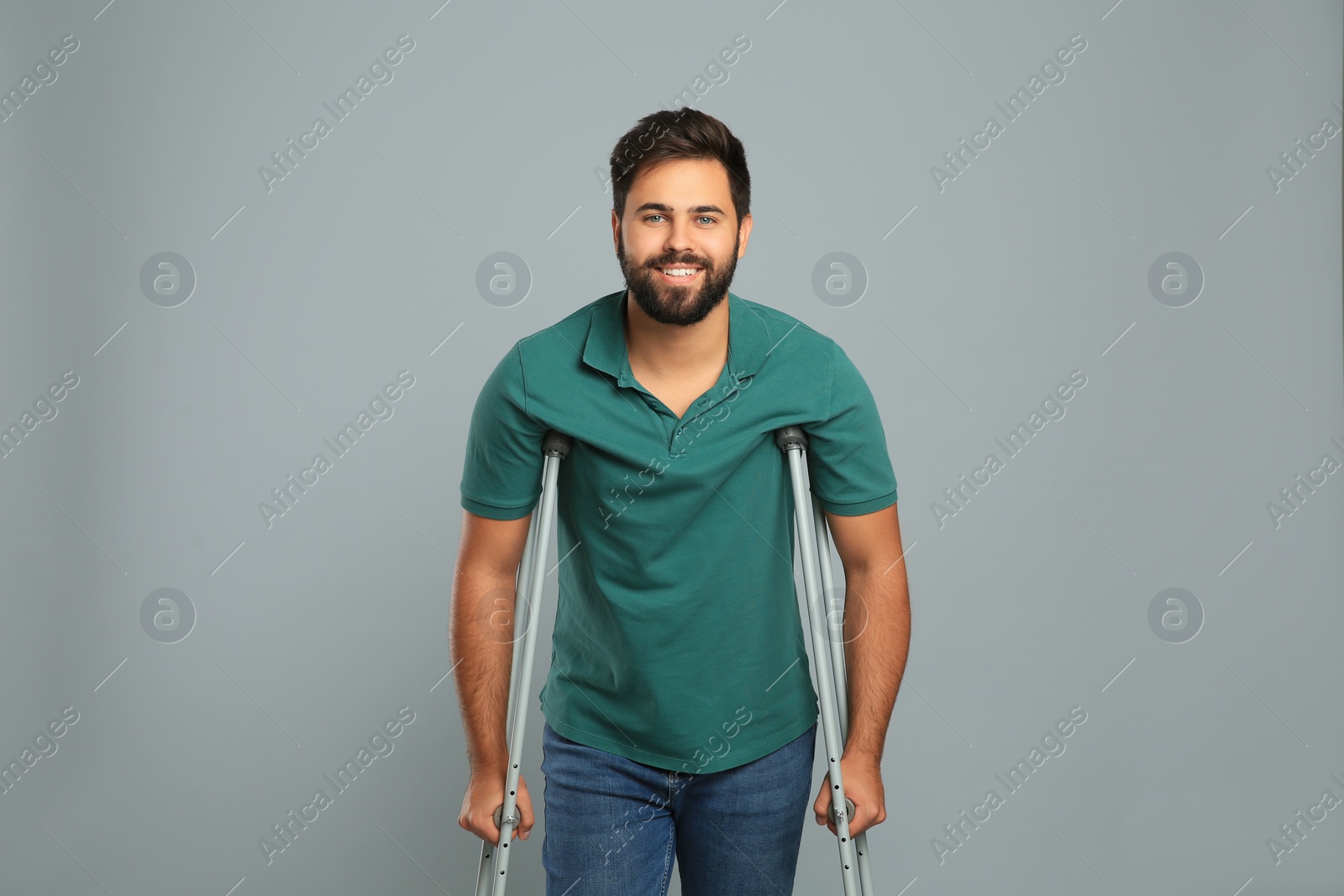 Photo of Young man with axillary crutches on grey background