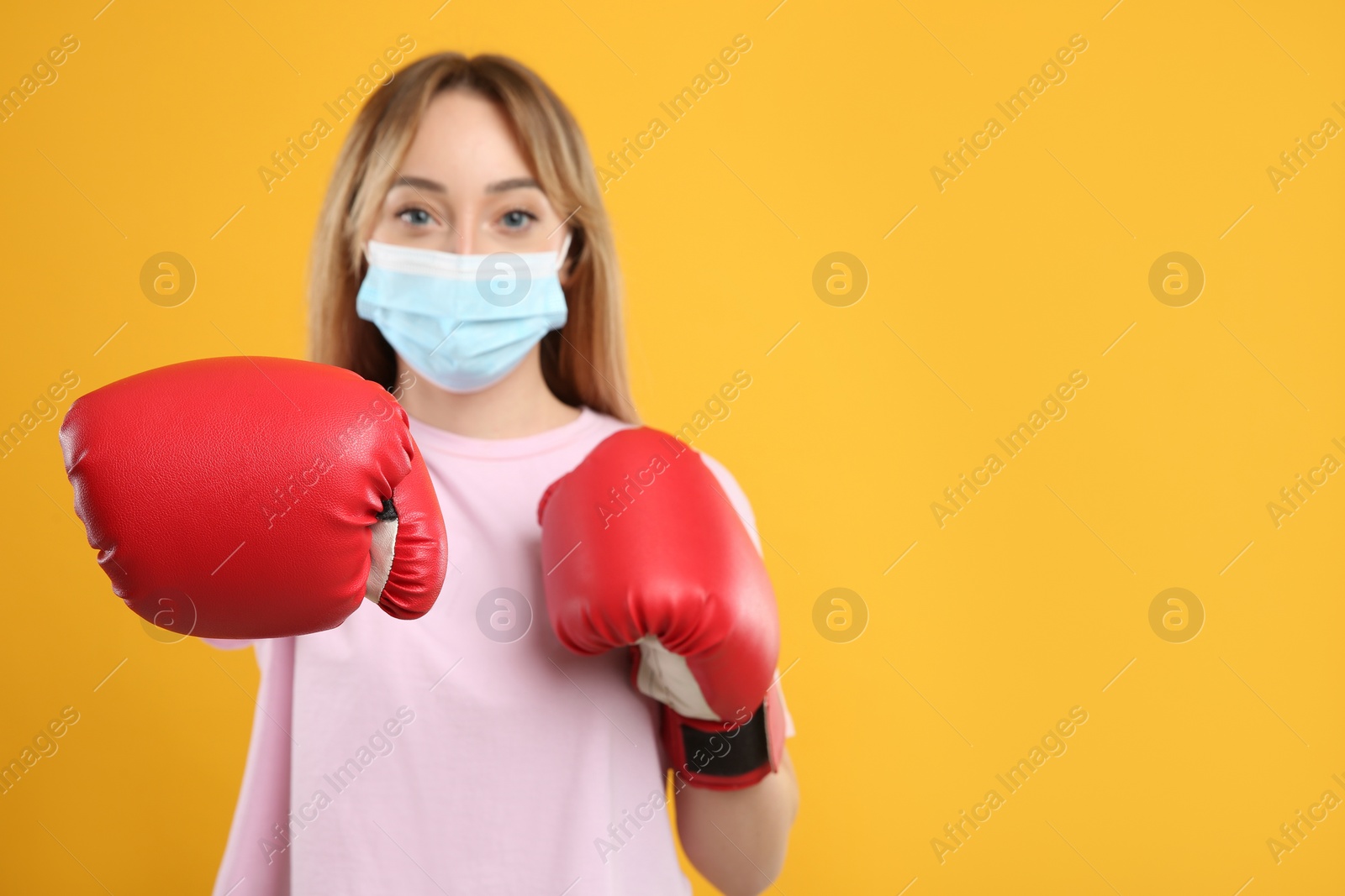 Photo of Woman with protective mask and boxing gloves on yellow background, space for text. Strong immunity concept