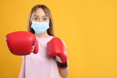 Photo of Woman with protective mask and boxing gloves on yellow background, space for text. Strong immunity concept