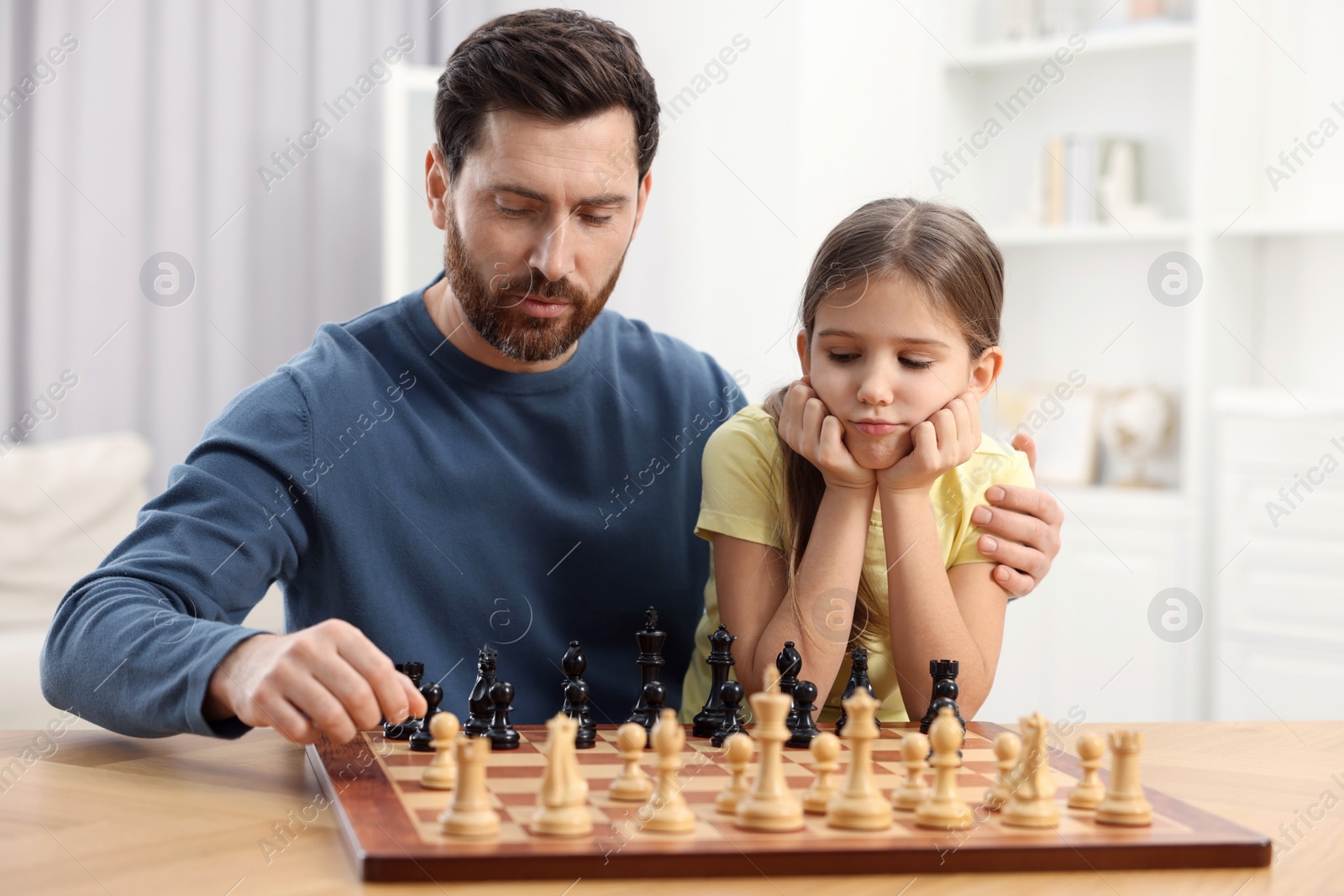 Photo of Father teaching his daughter to play chess at home