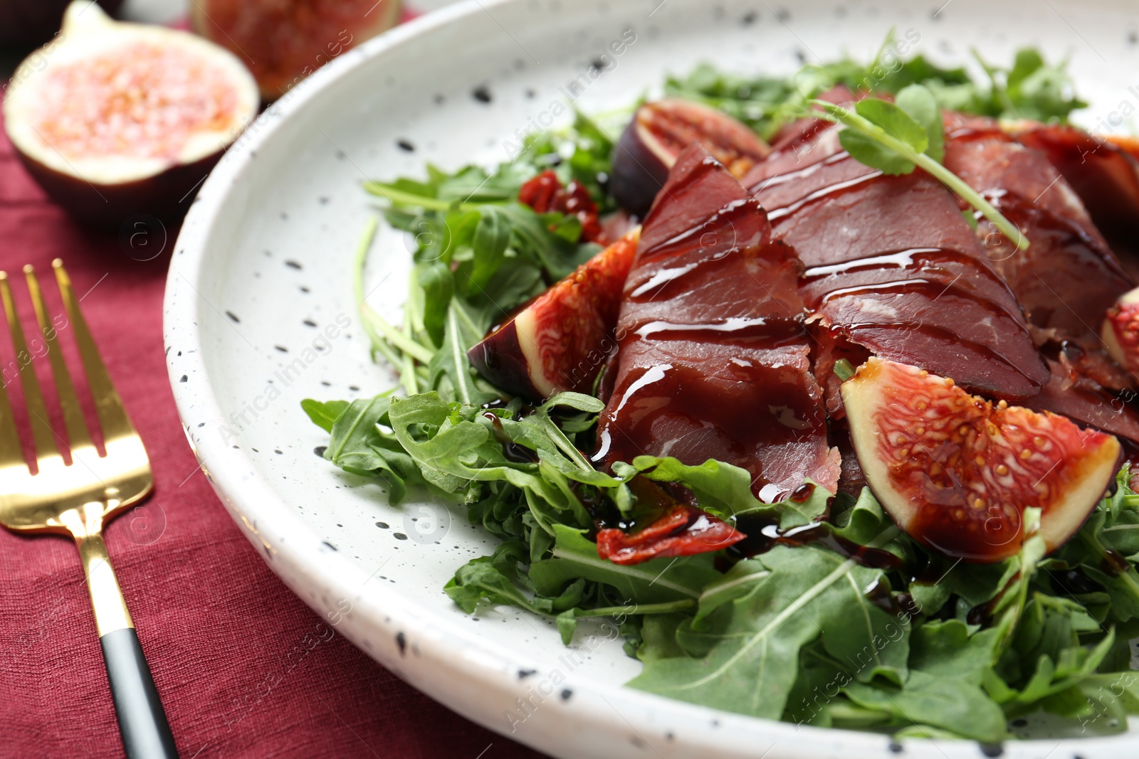 Photo of Plate of tasty bresaola salad with figs, sun-dried tomatoes, balsamic vinegar and fork on table, closeup