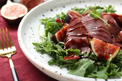 Plate of tasty bresaola salad with figs, sun-dried tomatoes, balsamic vinegar and fork on table, closeup