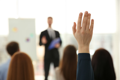 Photo of Young woman raising hand to ask question at business training indoors, closeup