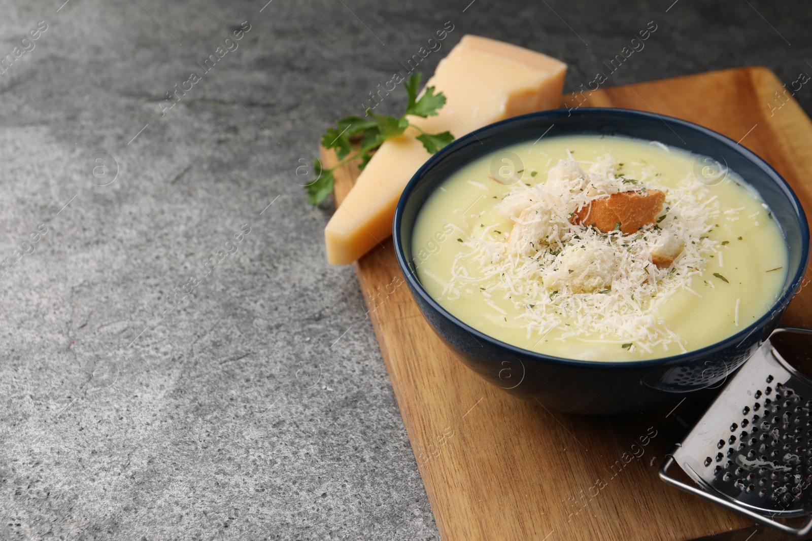 Photo of Delicious cream soup with parmesan cheese and croutons in bowl on grey table. Space for text