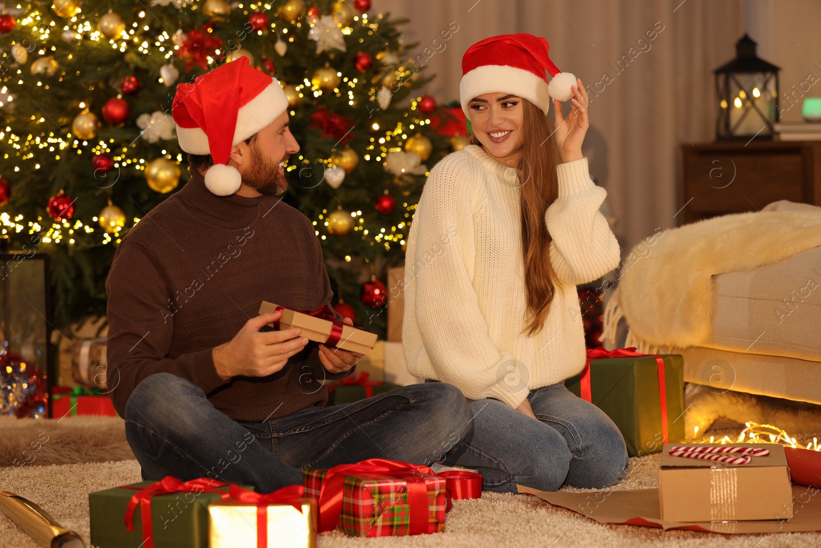 Photo of Happy couple in Santa hats with Christmas gifts at home