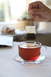 Photo of Woman taking tea bag out of cup at white wooden table indoors, closeup