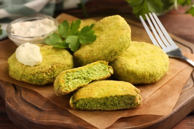 Photo of Tasty vegan cutlets served with sauce and parsley on wooden board, closeup