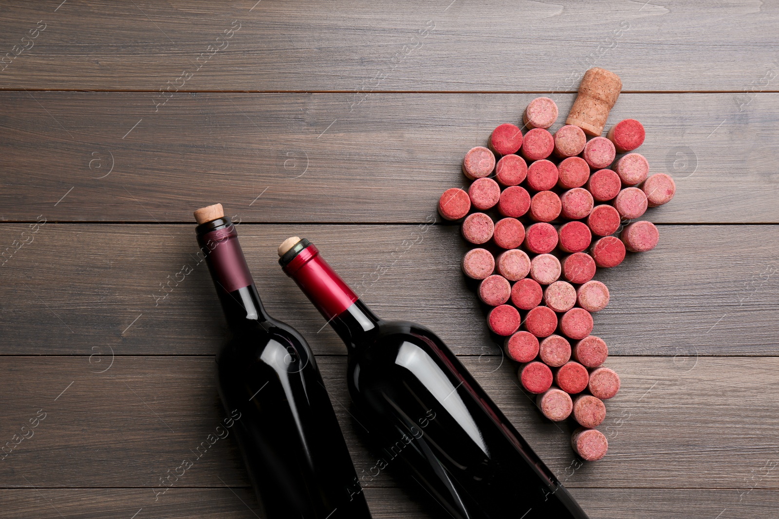 Photo of Grape made of wine corks and bottles on wooden table, flat lay