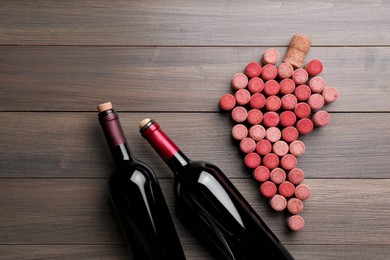 Photo of Grape made of wine corks and bottles on wooden table, flat lay