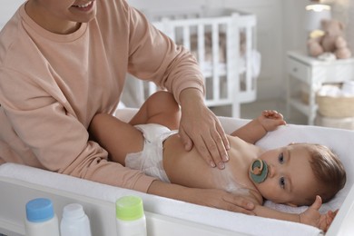 Photo of Mother applying dusting powder on her cute baby at home, closeup