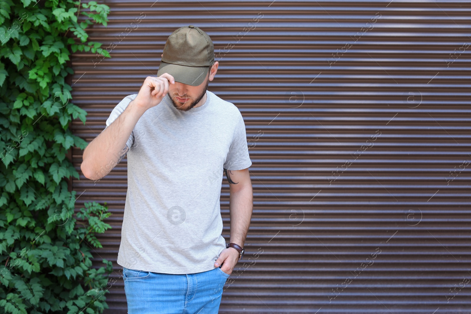 Photo of Young man wearing gray t-shirt near wall on street. Urban style