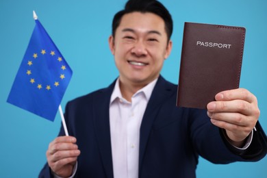 Photo of Immigration. Happy man with passport and flag of European Union on light blue background, selective focus