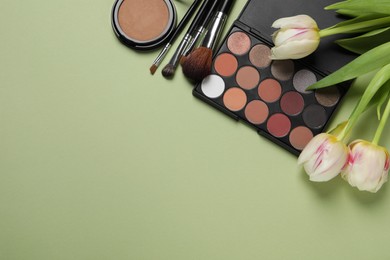 Photo of Flat lay composition with eyeshadow palette and beautiful flowers on pale olive background, space for text