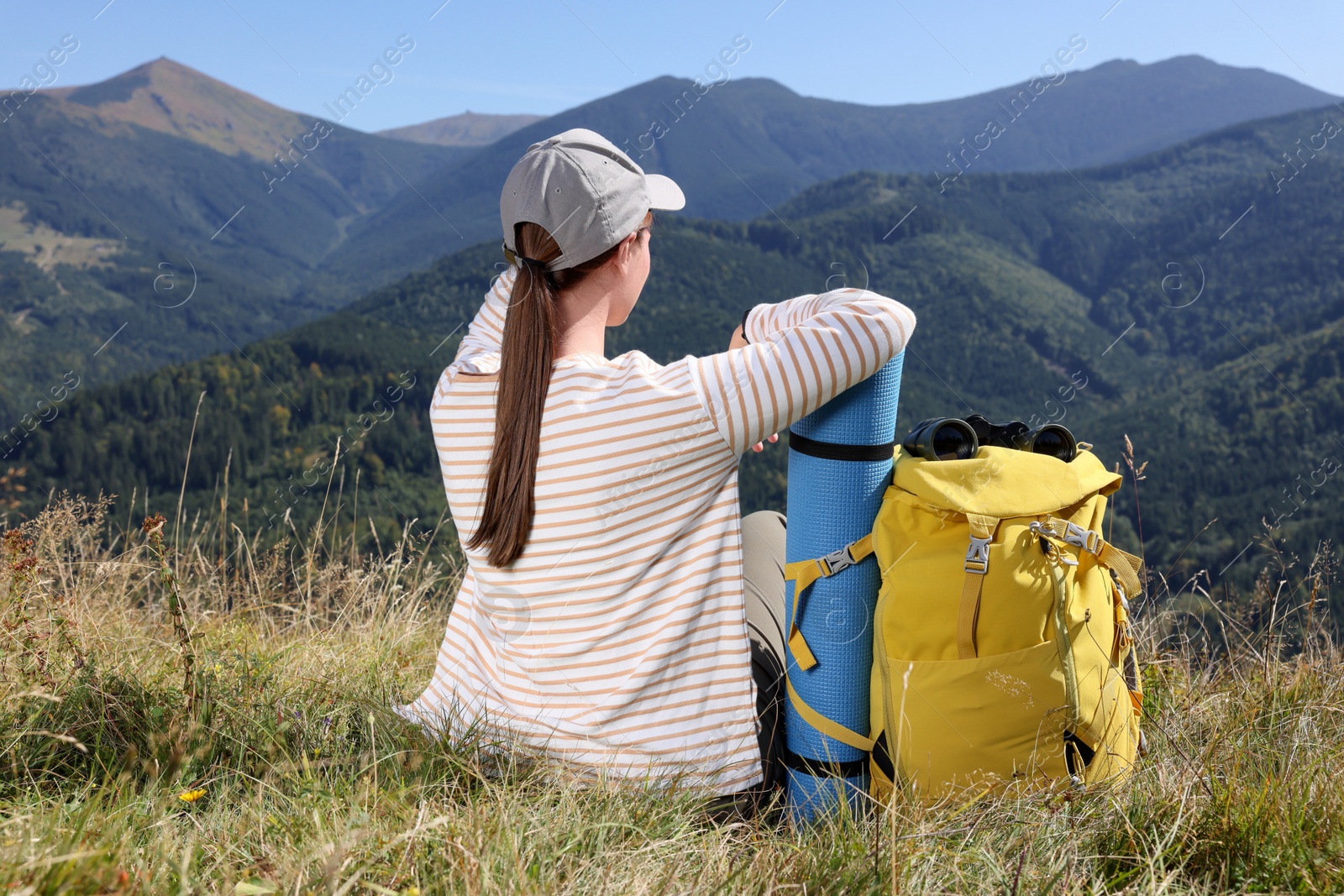 Photo of Tourist with backpack, sleeping pad and binoculars in mountains on sunny day