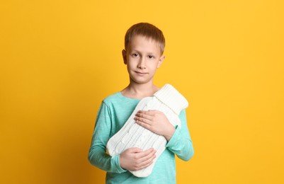 Photo of Ill boy with hot water bottle suffering from cold on yellow background