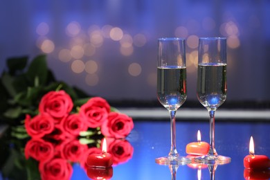 Glasses of champagne, candles and roses on table against blurred lights. Romantic dinner for Valentine's day