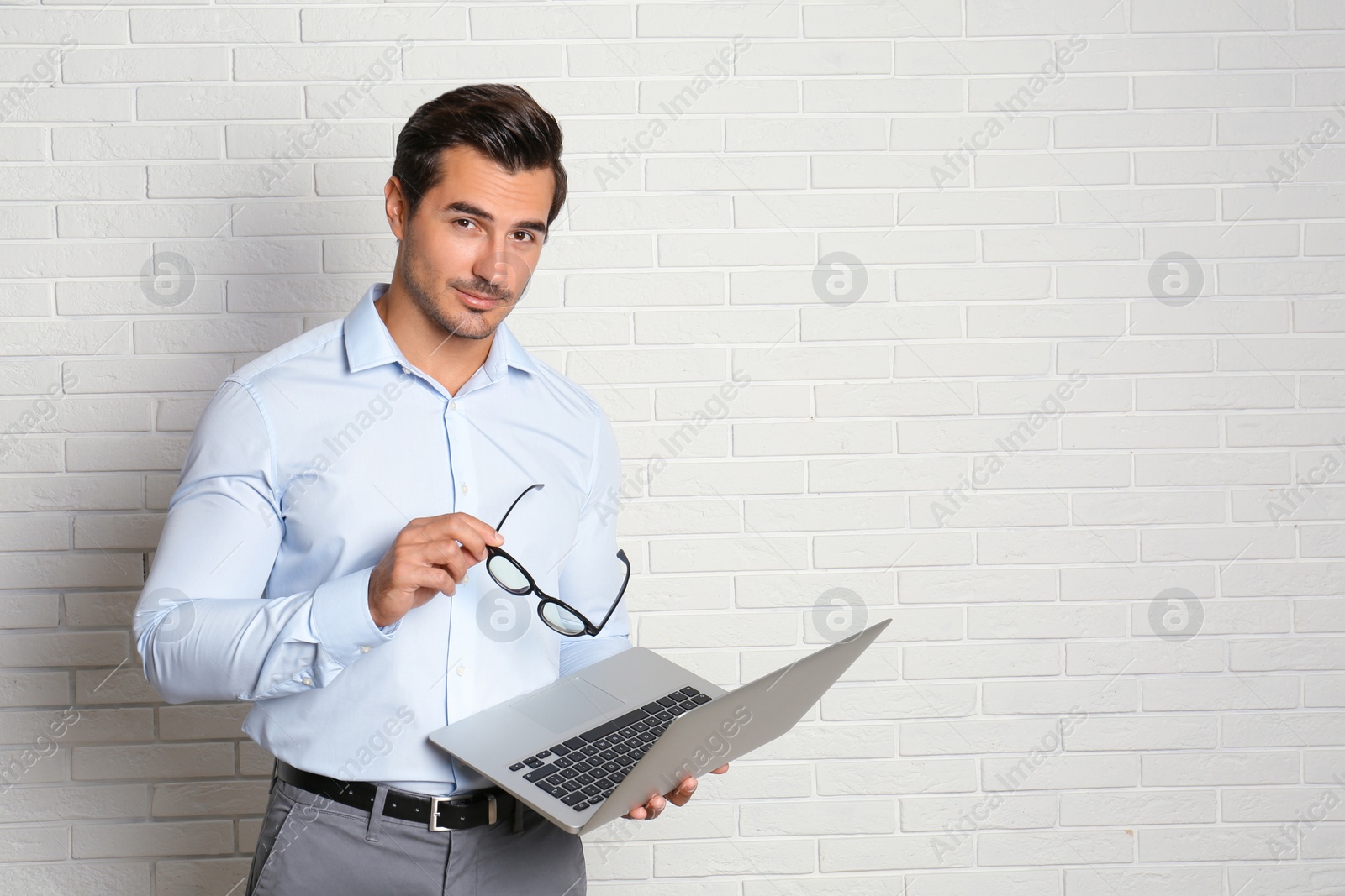 Photo of Young male teacher with glasses and laptop near brick wall. Space for text