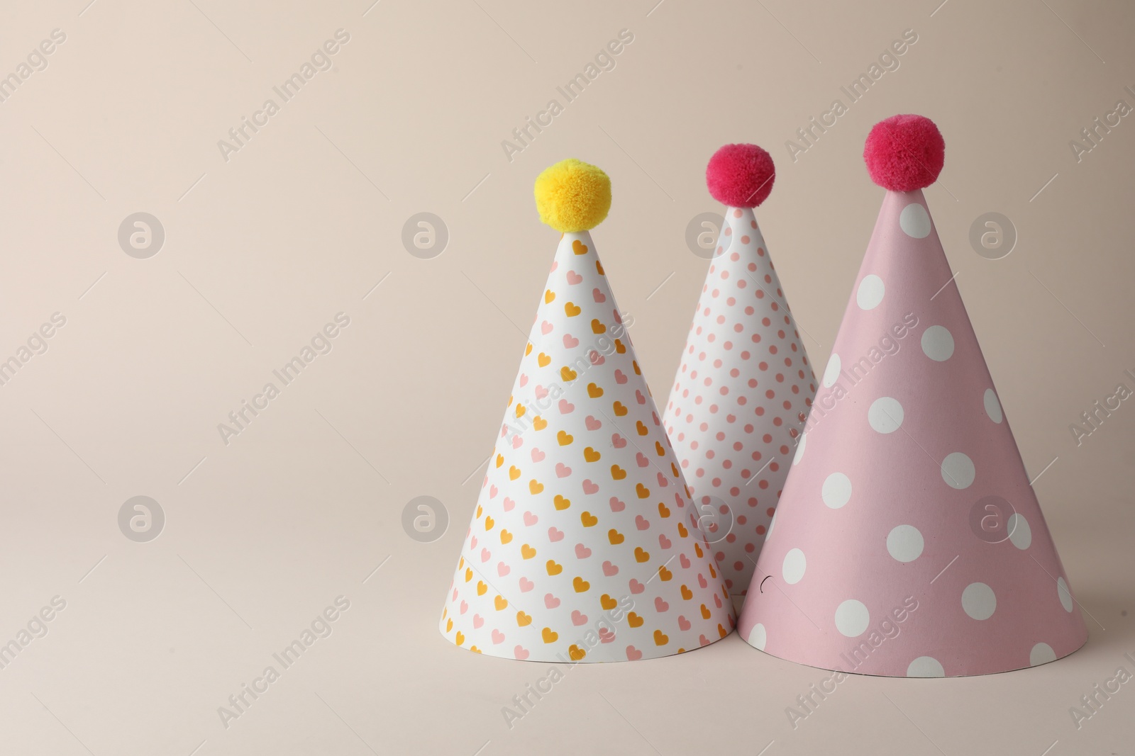 Photo of Beautiful party hats with pompoms on beige background. Space for text