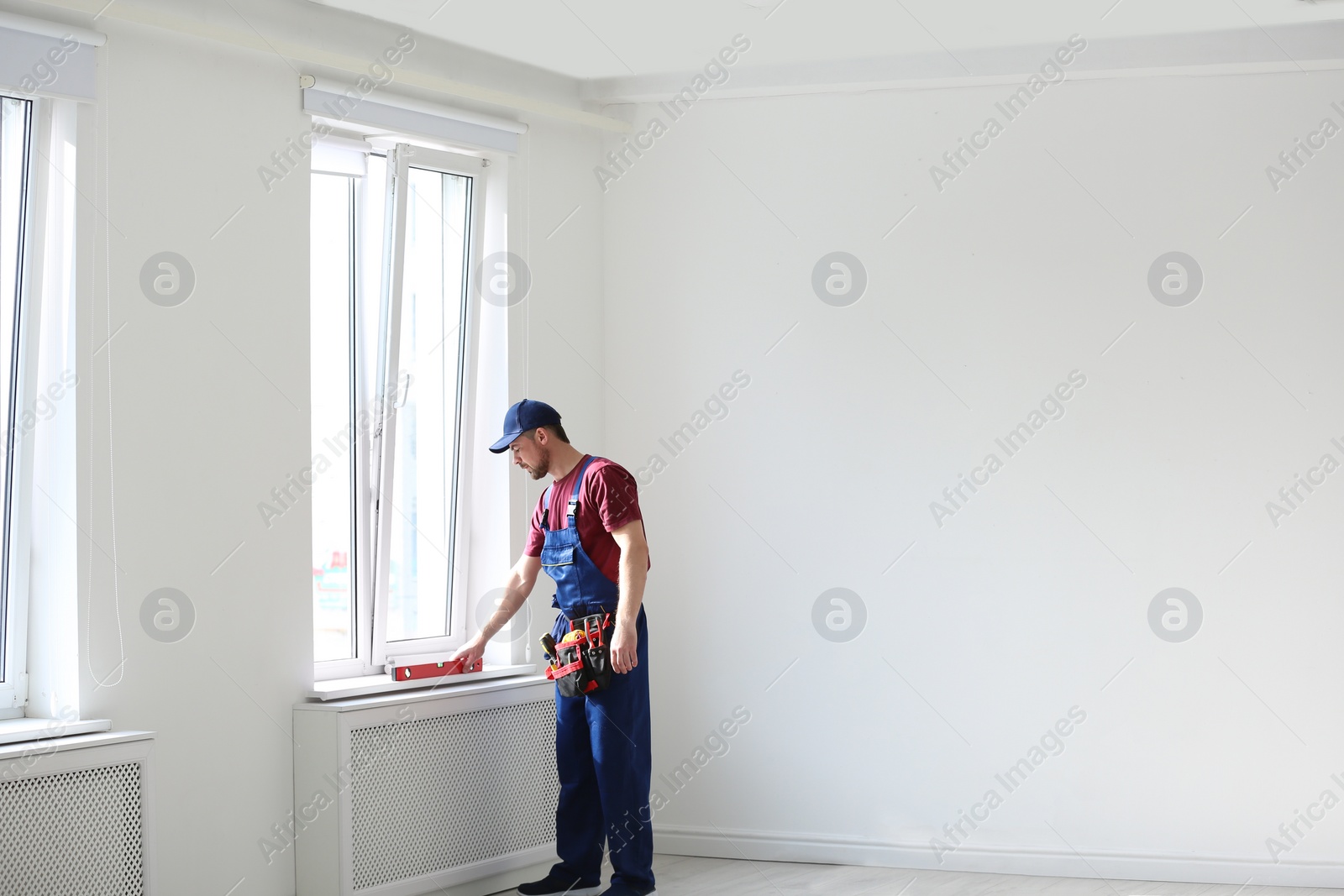 Photo of Handyman in uniform working with building level indoors, space for text. Professional construction tools