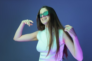 Portrait of beautiful young woman with sunglasses on color background with neon lights