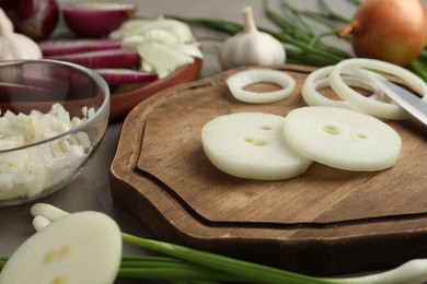 Photo of Fresh onion and wooden board on grey table, closeup