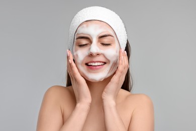 Photo of Young woman with headband washing her face on light grey background