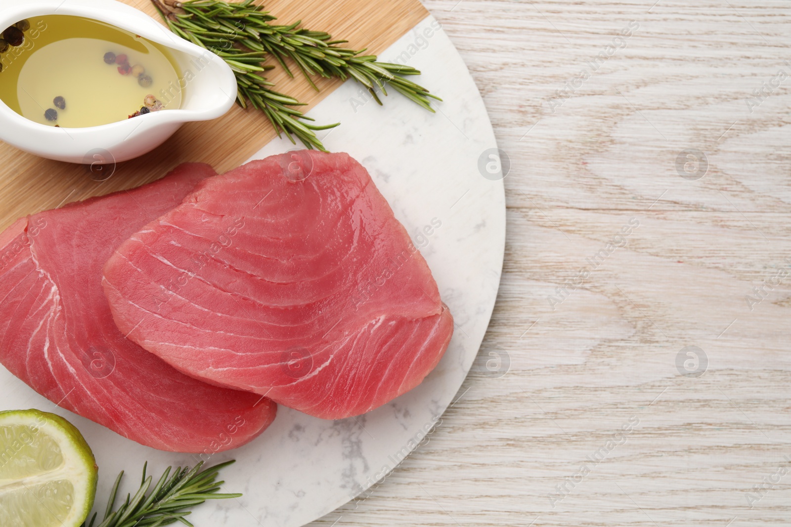 Photo of Raw tuna fillets with rosemary, lime and oil on white wooden table, top view