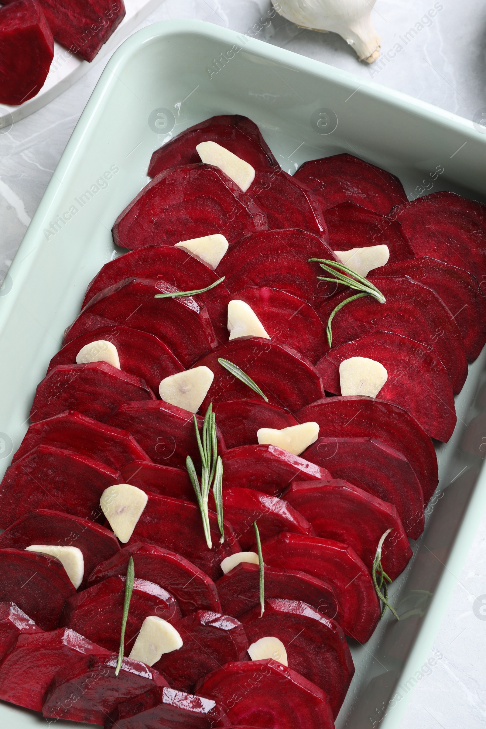 Photo of Baking dish with raw beetroot slices, garlic and rosemary on table, above view