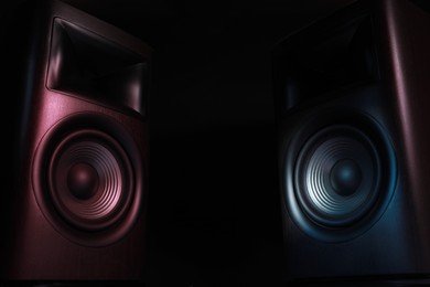 Photo of Modern sound speakers in neon light on black background. Space for text