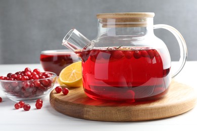 Photo of Tasty hot cranberry tea in teapot, lemon and fresh berries on white wooden table