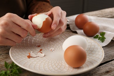 Photo of Woman peeling boiled egg at old wooden table, closeup