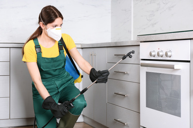 Pest control worker spraying pesticide in kitchen