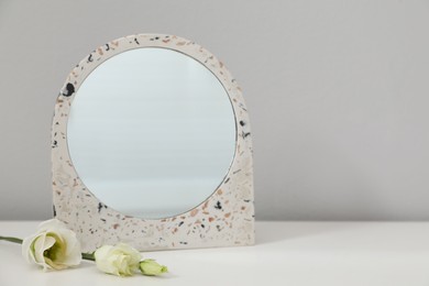 Photo of Stylish round mirror and flowers on table near white wall, space for text