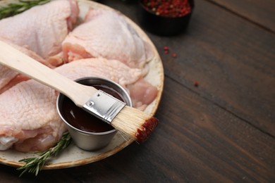 Photo of Plate with marinade, raw chicken and basting brush on wooden table, closeup. Space for text