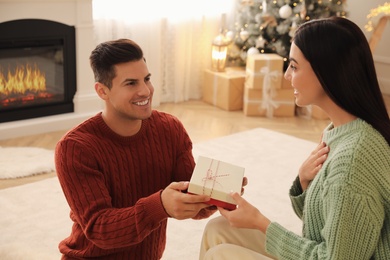 Photo of Boyfriend giving Christmas gift box to his girlfriend in living room