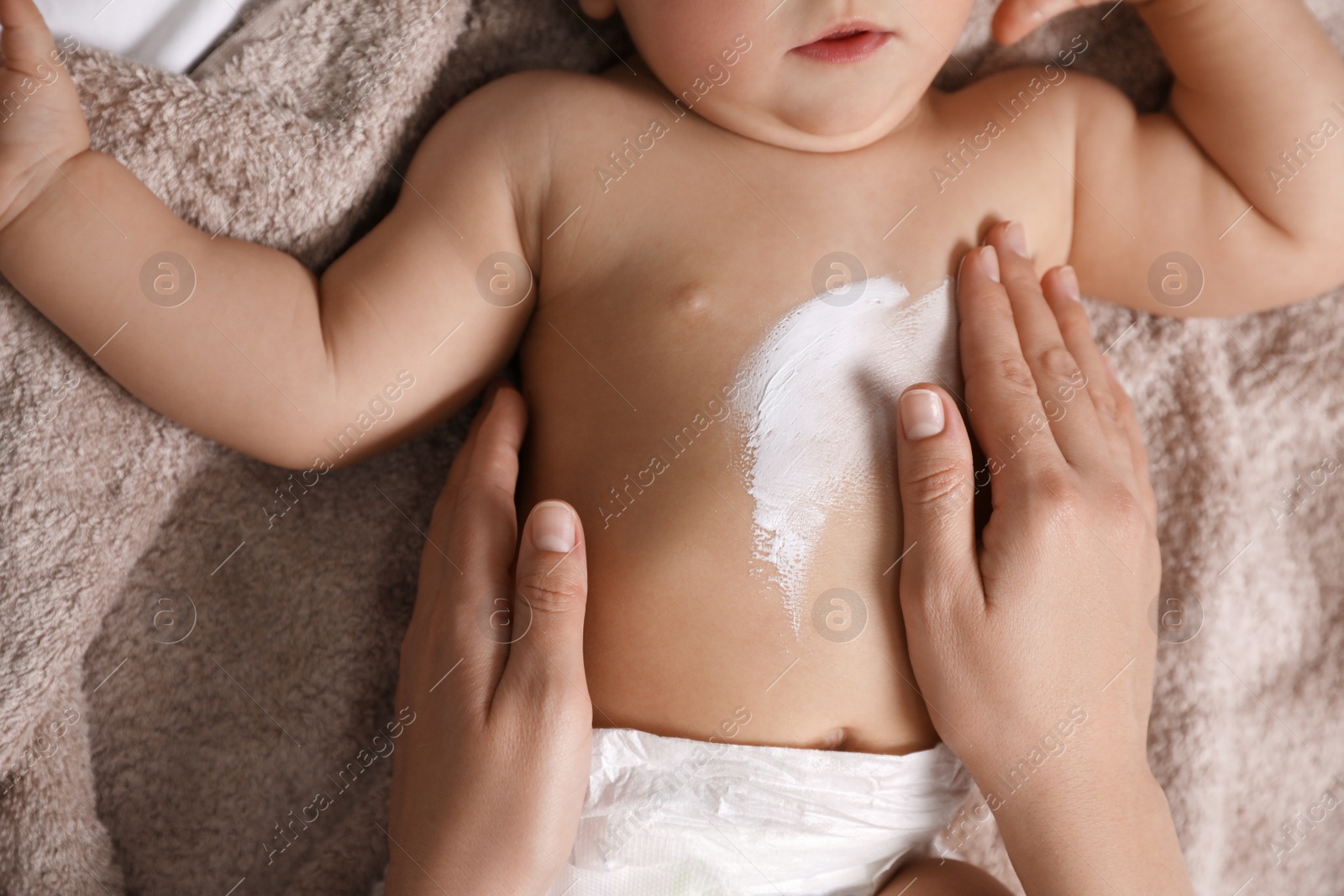 Photo of Mother applying moisturizing cream onto her little baby's skin on towel, closeup