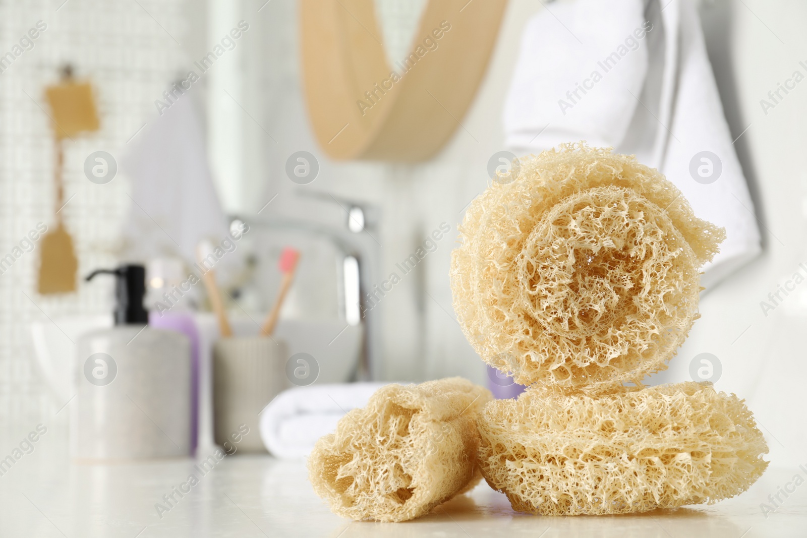 Photo of Natural loofah sponges on table in bathroom. Space for text