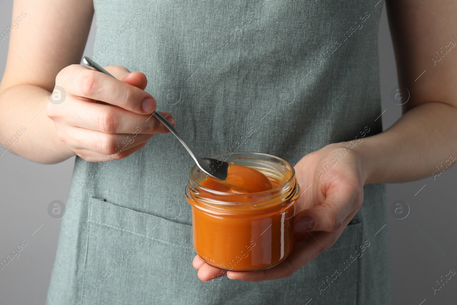 Photo of Woman with delicious persimmon jam on gray background, closeup
