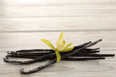 Photo of Vanilla pods and beautiful flower on white wooden table, closeup. Space for text