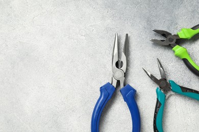 Photo of Different pliers on grey textured table, flat lay. Space for text