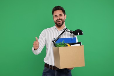 Photo of Happy unemployed man with box of personal office belongings showing thumb up on green background