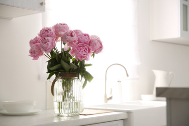 Vase with bouquet of beautiful pink peonies in kitchen. Space for text