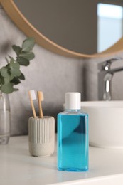 Bottle of mouthwash and toothbrushes on white countertop in bathroom