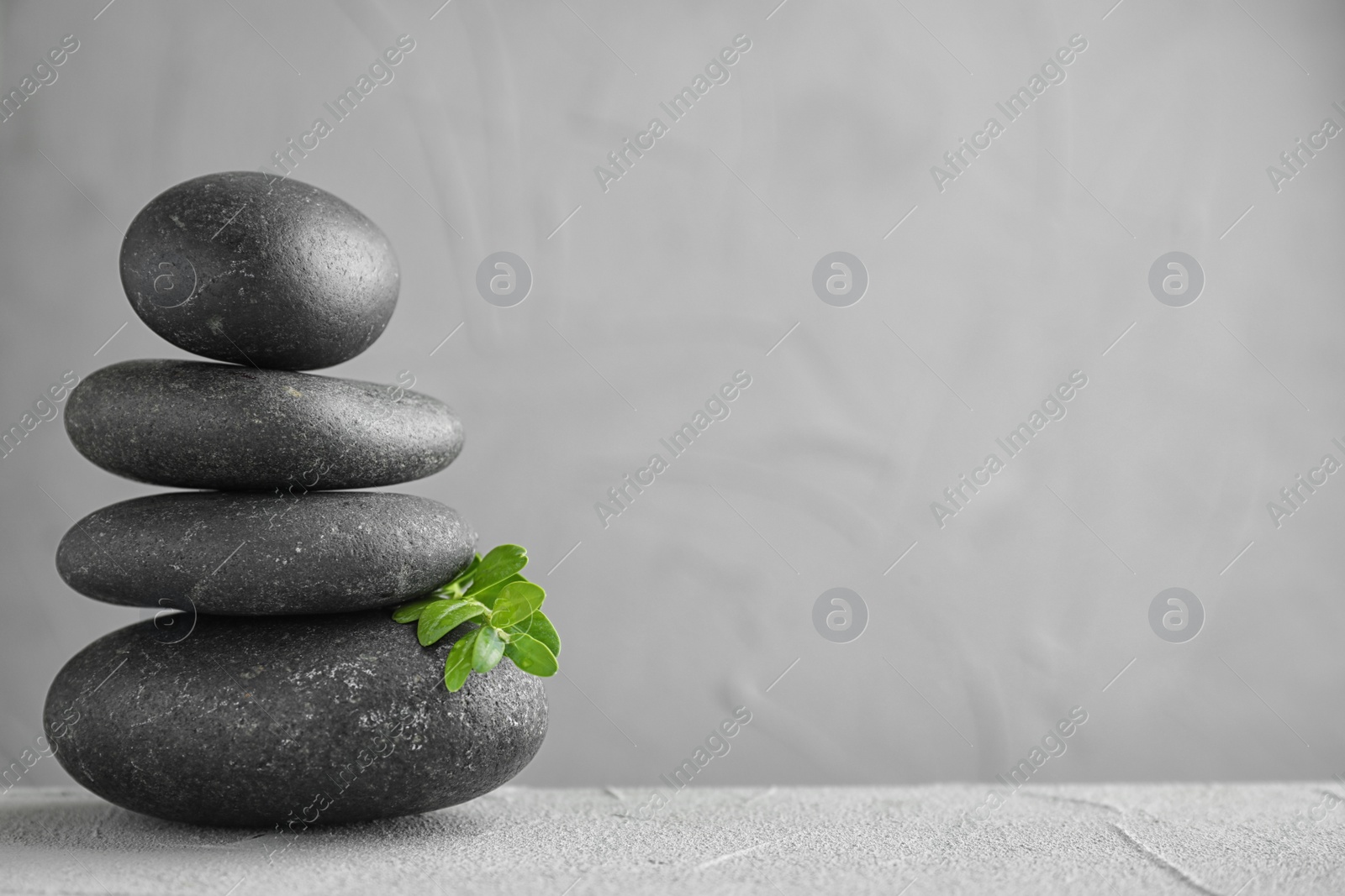 Photo of Stack of spa stones and green leaves on grey table, space for text