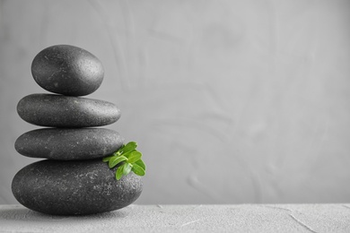 Photo of Stack of spa stones and green leaves on grey table, space for text