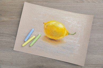 Photo of Beautiful drawing of lemon and pastels on wooden table, top view